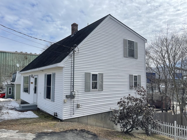 view of side of home featuring a shingled roof, a chimney, and fence