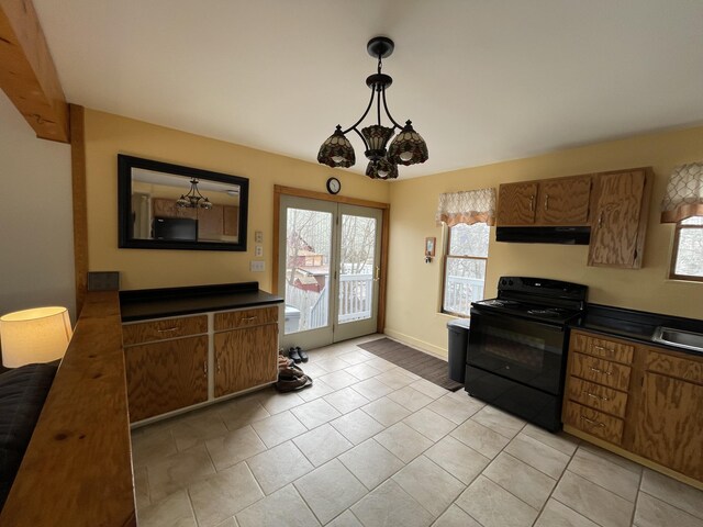 kitchen featuring black / electric stove, brown cabinetry, dark countertops, and under cabinet range hood