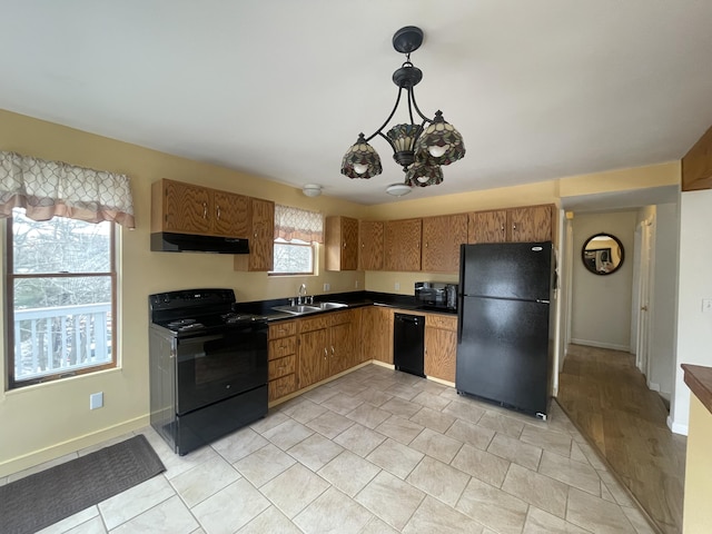 kitchen with dark countertops, a sink, under cabinet range hood, black appliances, and a wealth of natural light