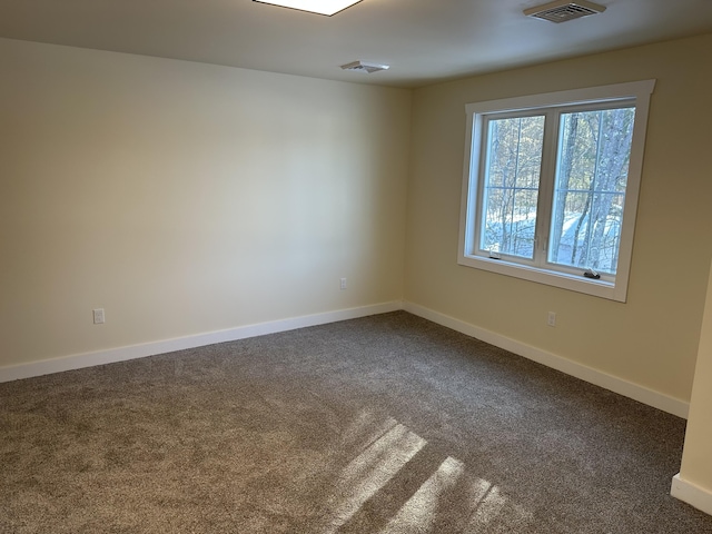 spare room featuring baseboards, visible vents, and dark carpet