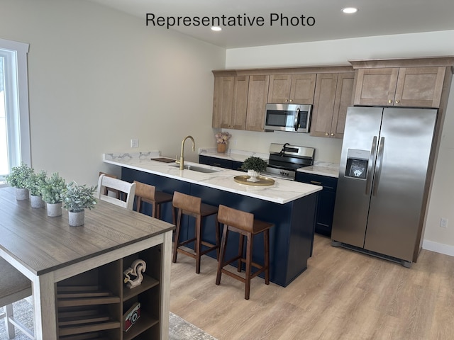 kitchen featuring light wood-type flooring, stainless steel appliances, a sink, and a kitchen breakfast bar