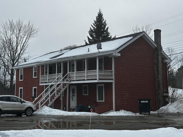 snow covered back of property featuring a chimney and stairs