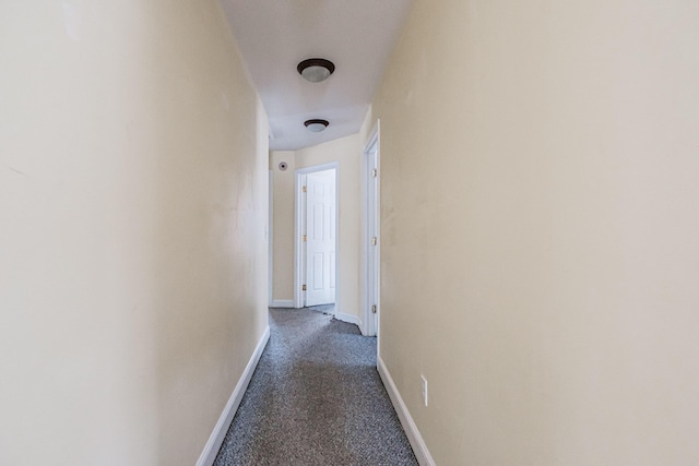 corridor featuring dark carpet and baseboards