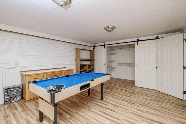 recreation room featuring wooden walls, a barn door, a paneled ceiling, and light wood-style floors