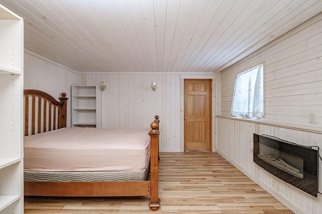 bedroom with a glass covered fireplace, wood ceiling, and wood finished floors