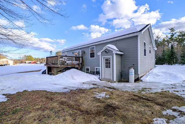 snow covered rear of property featuring a deck and roof mounted solar panels