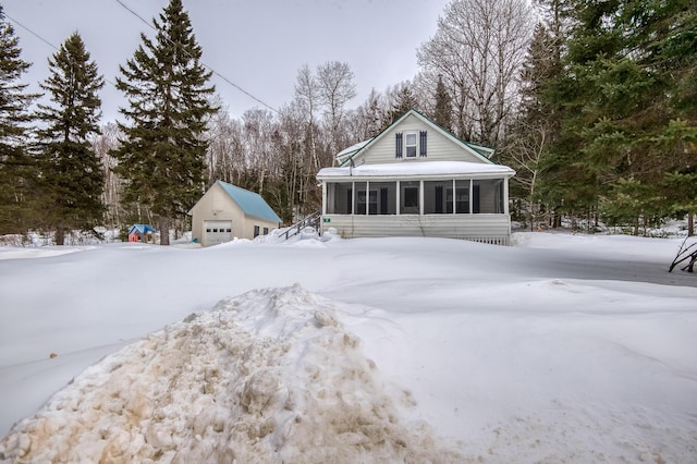 snow covered house featuring an outbuilding, a detached garage, and a sunroom