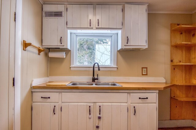 kitchen with white cabinetry, visible vents, a sink, and ornamental molding