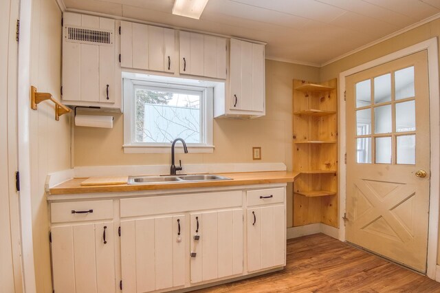 kitchen with light wood-style flooring, ornamental molding, light countertops, and a sink