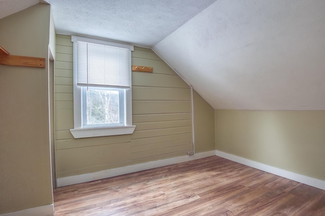 bonus room featuring a textured ceiling, vaulted ceiling, wood finished floors, and baseboards