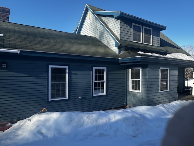 view of snowy exterior featuring roof with shingles