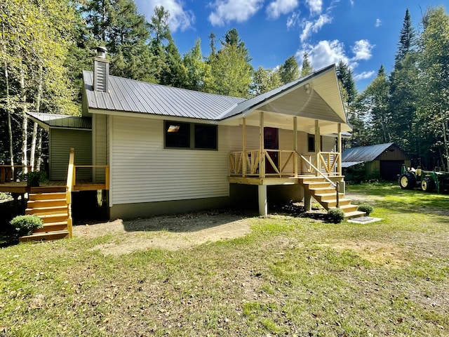 back of house with metal roof, covered porch, stairway, a lawn, and a chimney