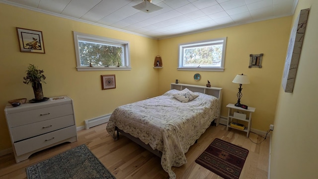 bedroom with light wood finished floors, a baseboard radiator, baseboards, and crown molding