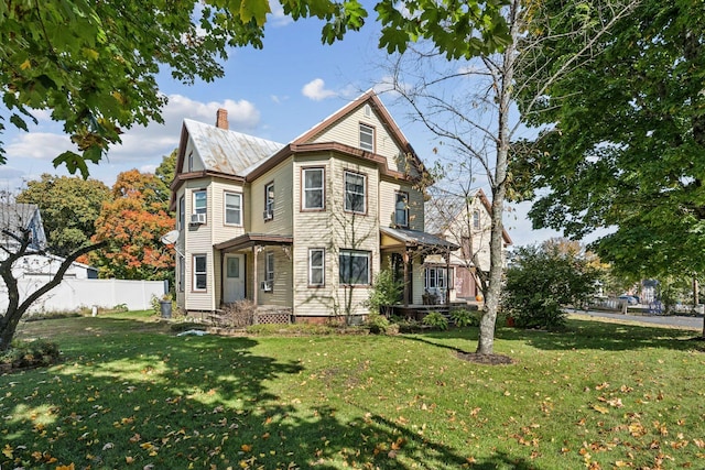 victorian home featuring a front lawn, a chimney, and fence