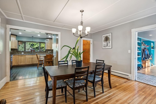 dining space with a baseboard heating unit, crown molding, light wood-style flooring, and an inviting chandelier