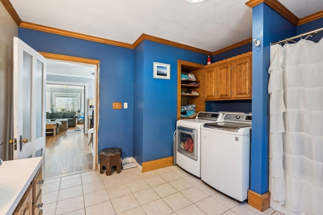 laundry area with light tile patterned floors, cabinet space, ornamental molding, washer and dryer, and baseboards