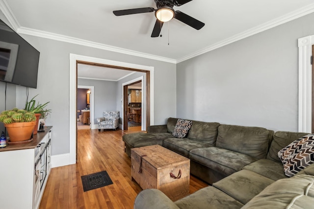 living room with crown molding, visible vents, light wood-style floors, ceiling fan, and baseboards