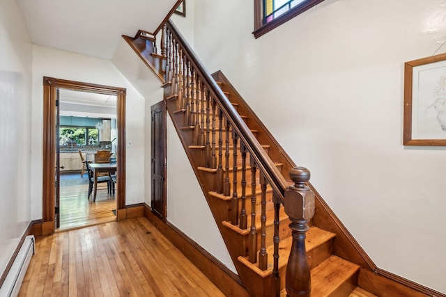 staircase featuring a baseboard radiator, baseboards, and hardwood / wood-style flooring