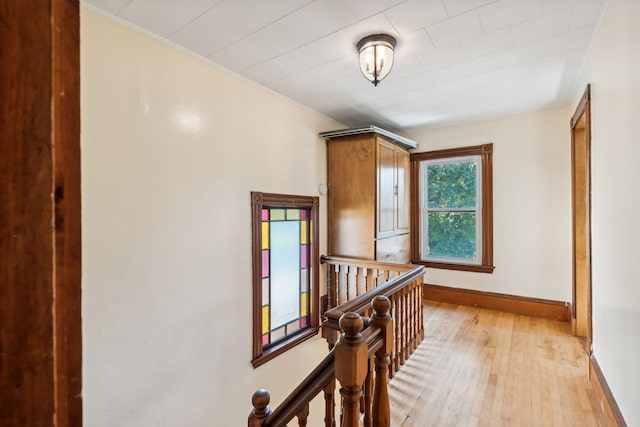 hallway with light wood finished floors, baseboards, and an upstairs landing