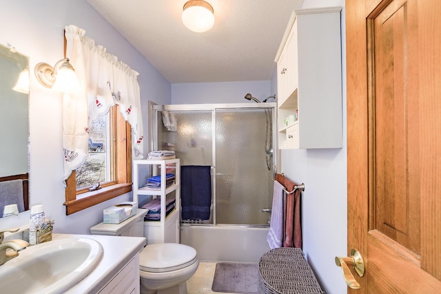 bathroom with combined bath / shower with glass door, toilet, vanity, and a textured ceiling