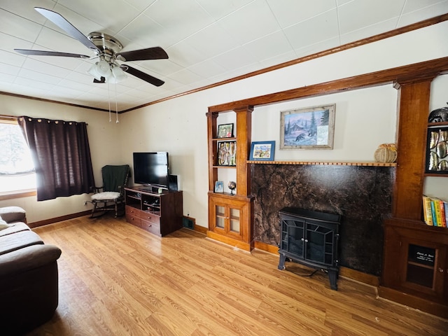 living room featuring crown molding, ceiling fan, baseboards, a wood stove, and wood finished floors