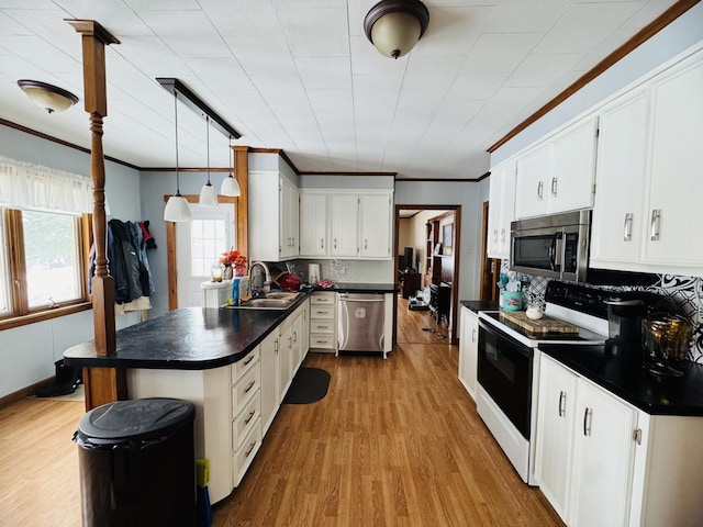 kitchen with a peninsula, a sink, stainless steel appliances, crown molding, and dark countertops