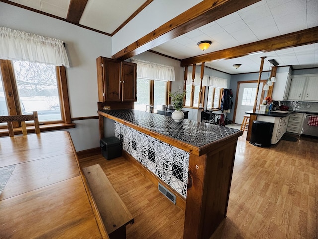 kitchen featuring visible vents, beam ceiling, dark countertops, light wood finished floors, and dishwasher