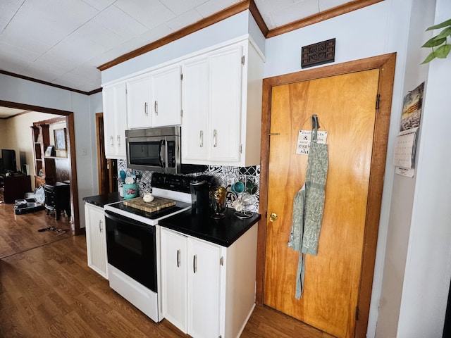 kitchen with dark countertops, crown molding, range with electric stovetop, white cabinetry, and stainless steel microwave