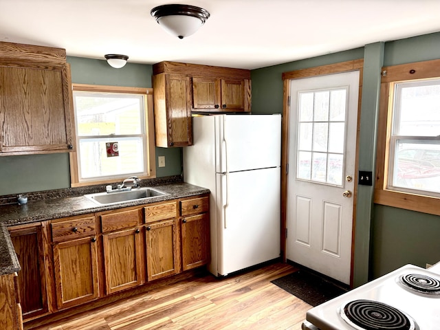 kitchen with dark countertops, brown cabinetry, light wood-style floors, a sink, and white appliances