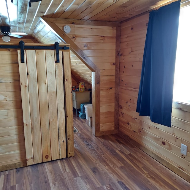 additional living space featuring wood walls, wood ceiling, a barn door, vaulted ceiling, and wood finished floors