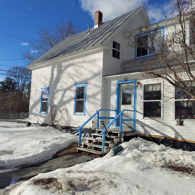 snow covered back of property featuring a standing seam roof, metal roof, and a chimney