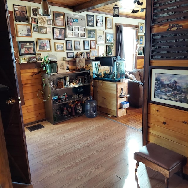 interior space featuring beam ceiling, wooden walls, wood finished floors, and visible vents