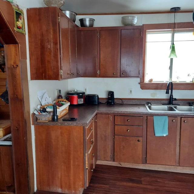 kitchen with a sink, brown cabinets, pendant lighting, and dark wood-style floors