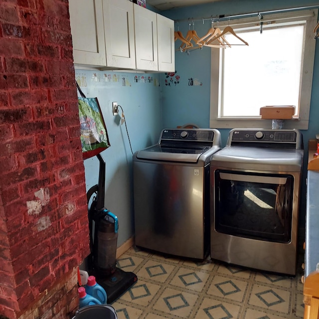 washroom with washer and dryer, cabinet space, light floors, and brick wall