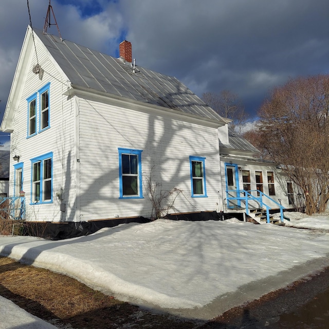 rear view of property featuring a chimney, a standing seam roof, and metal roof