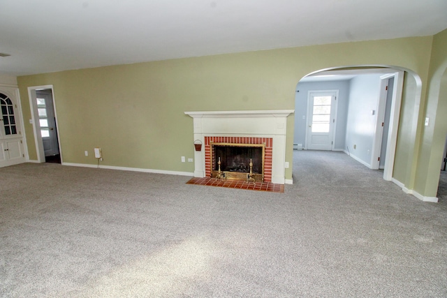 unfurnished living room featuring carpet floors, arched walkways, a brick fireplace, and baseboards