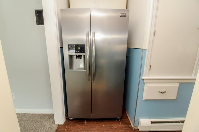 kitchen with a baseboard heating unit, stainless steel fridge, white cabinetry, and baseboards