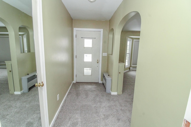 carpeted foyer featuring radiator heating unit, arched walkways, baseboard heating, and baseboards