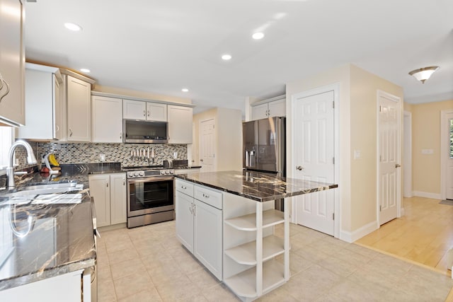 kitchen with tasteful backsplash, a sink, dark stone countertops, appliances with stainless steel finishes, and open shelves