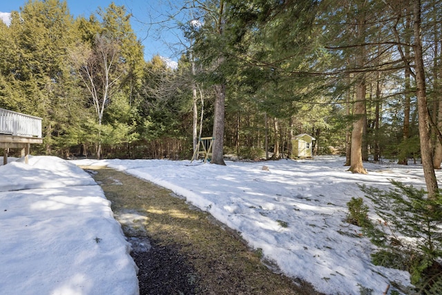 yard covered in snow with an outdoor structure, a wooded view, and a shed