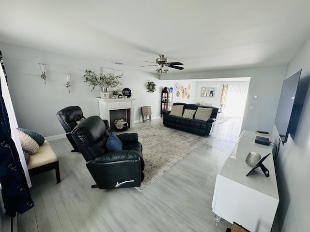 living room featuring ceiling fan, a fireplace, baseboards, and wood finished floors