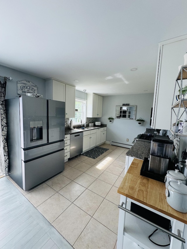 kitchen with dark countertops, appliances with stainless steel finishes, a baseboard heating unit, light tile patterned flooring, and a sink