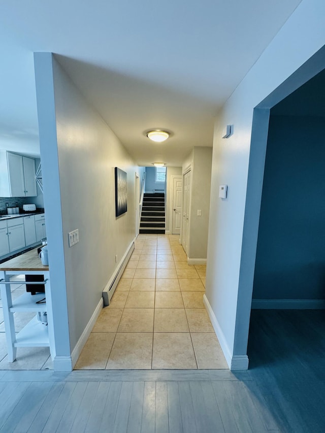 hall with stairs, a baseboard radiator, light tile patterned flooring, and baseboards