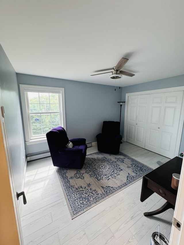 living room with light wood finished floors, a baseboard heating unit, and a ceiling fan