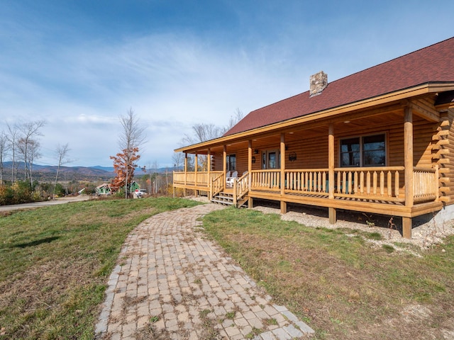 log home featuring a chimney, a porch, a mountain view, log exterior, and a front lawn