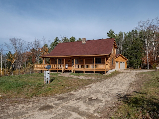 cabin featuring an outbuilding, covered porch, a garage, driveway, and log siding