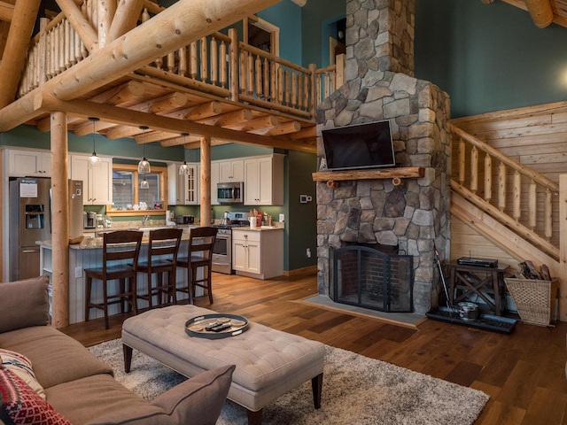 living room featuring stairs, a stone fireplace, a towering ceiling, and light wood-style floors