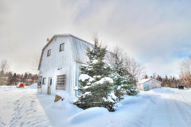 view of snowy exterior featuring an outbuilding, board and batten siding, and a gambrel roof