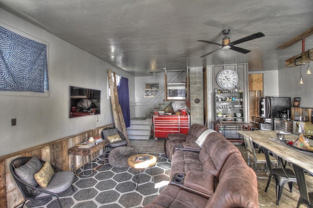 living area with a wainscoted wall, stairway, and a ceiling fan