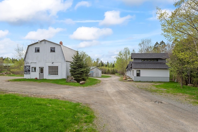 2342 Main St, Rangeley, ME 04970 - view of home's exterior featuring an outdoor structure, dirt driveway, a gambrel roof, a chimney, and a detached garage